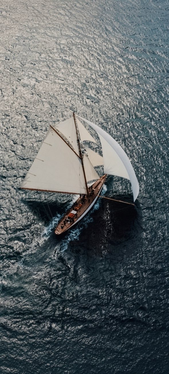 A classic yacht under sail seen from above on dark teal water